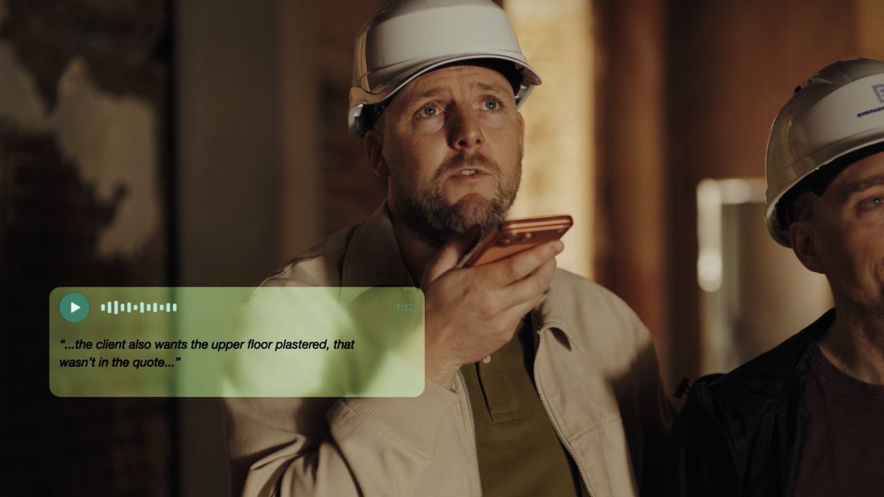A project leader in a white hard hat records a voice memo on site: “…the client also wants the upper floor plastered, that wasn’t in the quote…”